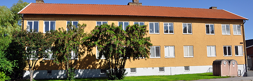 Gult tvåvåningshus med träd framför